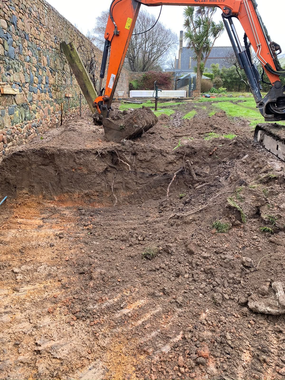 Mini-digger reducing ground levels alongside the existing stone wall