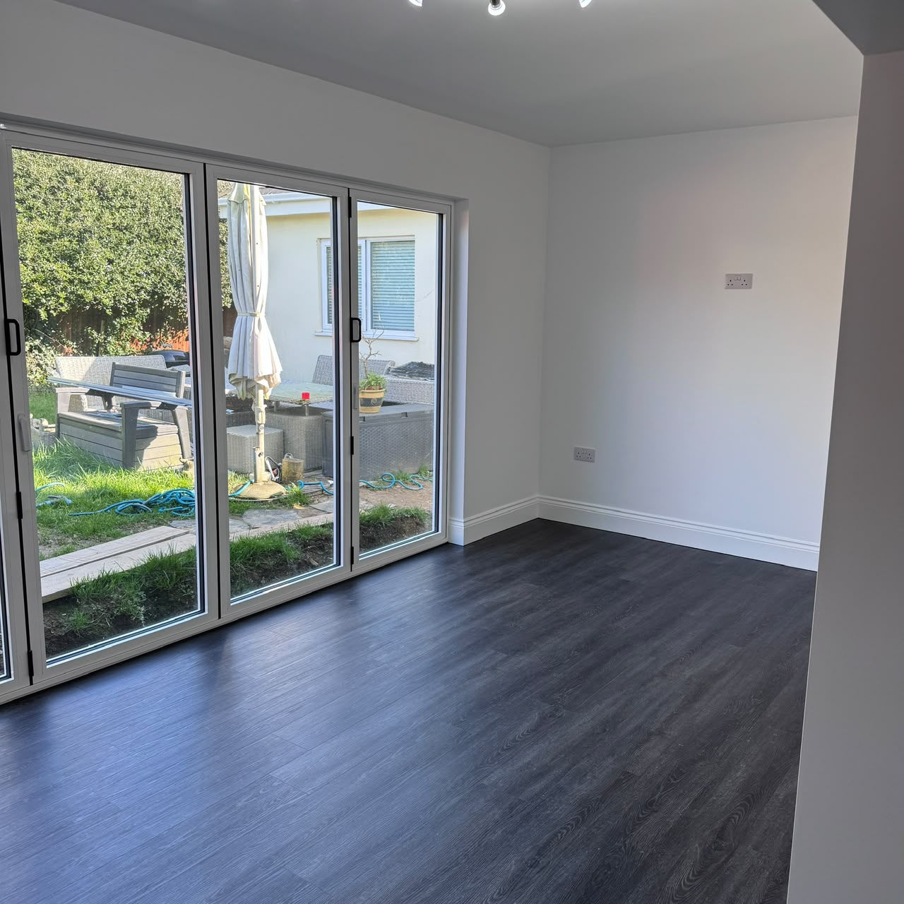 Completed single-storey dining extension with dark laminate floor and bifold doors — Guernsey